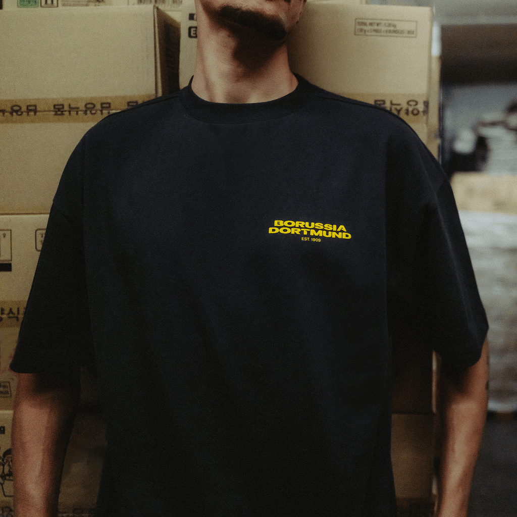 アントラサイト色の「BVB Urban」Tシャツ。黄色いボルシア・ドルトムントのロゴと「EST 1909」の文字が入っており、同クラブのファンに最適です。
