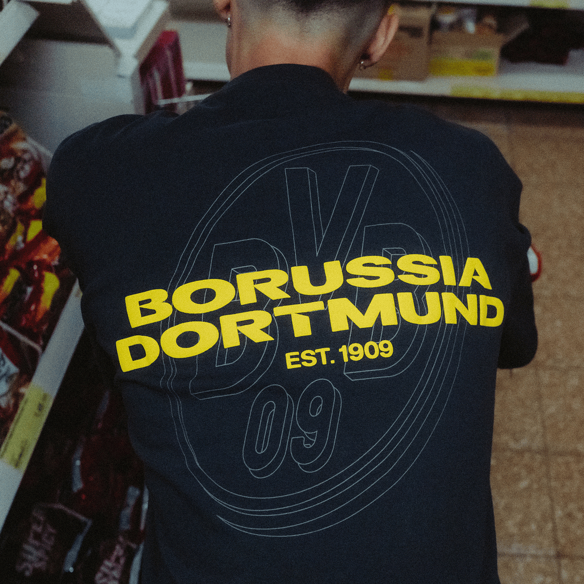 Vista posteriore di una maglietta nera BVB Urban con il logo giallo del Borussia Dortmund e la scritta “EST. 1909”, articolo per i tifosi della stagione 2025.
