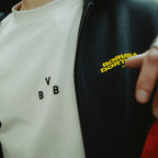 Beiges BVB Urban Tee 2025 mit schwarzem BVB-Logo, kombiniert mit einer schwarzen Jacke mit gelbem Borussia Dortmund Schriftzug.