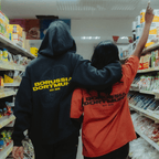 一家商店里有两个人，其中一人背对着镜头，穿着一件黑色多特蒙德（BVB）连帽衫，另一人则穿着一件印有“多特蒙德”字样的橙色Urban T恤。