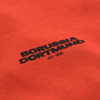 一件橙色BVB Urban连帽衫的特写，上面印有黑色的“Borussia Dortmund”字样和“EST. 1909”标志。