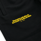 Black BVB Urban sweatpants featuring a yellow Borussia Dortmund logo and "EST. 1909" lettering in close-up, perfect for fans and casual wear.