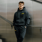 Black BVB Urban sweatpants with a yellow Borussia Dortmund logo, paired with a matching hoodie, shown in an urban setting.