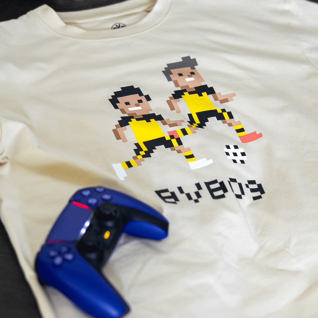 Off-white T-shirt for kids featuring a pixelated design of two figures in black-and-yellow jerseys and "BVB 09" lettering, perfect for gaming and soccer fans.