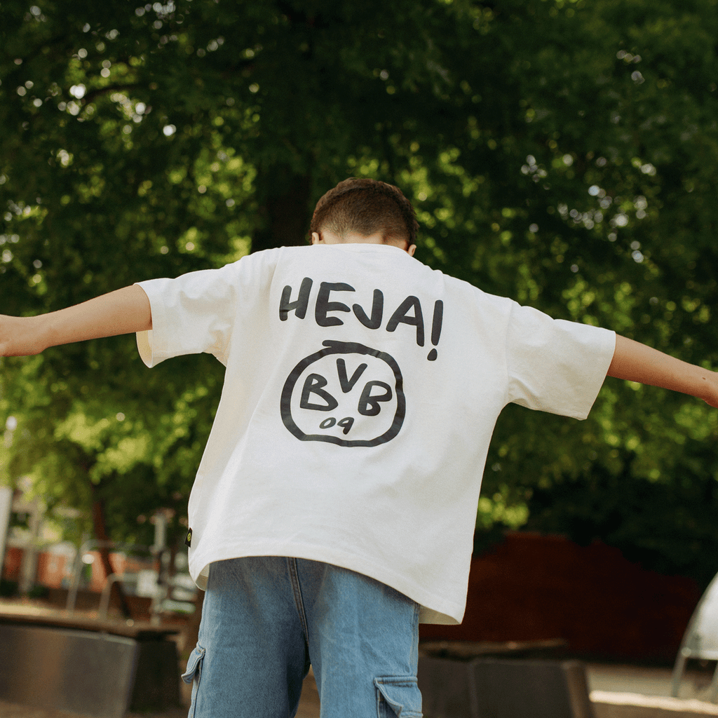 T-shirt blanc pour enfant du BVB, orné de l'inscription « HEJA » en noir et du logo du BVB au dos, porté par un enfant à l'extérieur.