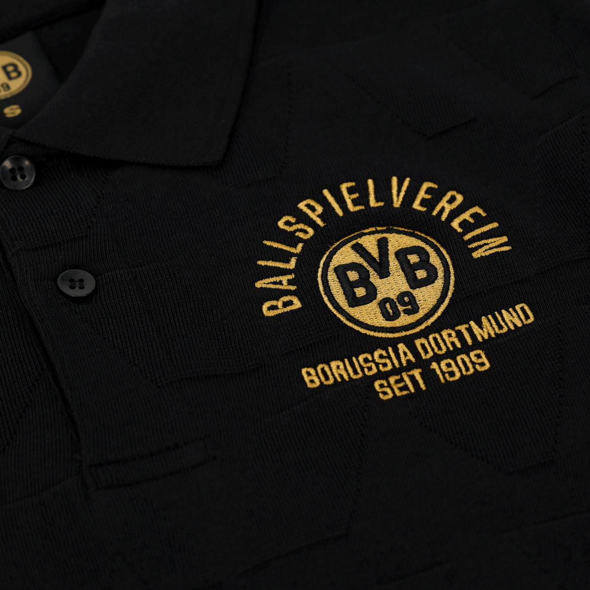Polo nera del BVB della collezione di articoli per i tifosi, con logo della società e scritta ricamati in giallo, per i tifosi del Borussia Dortmund.