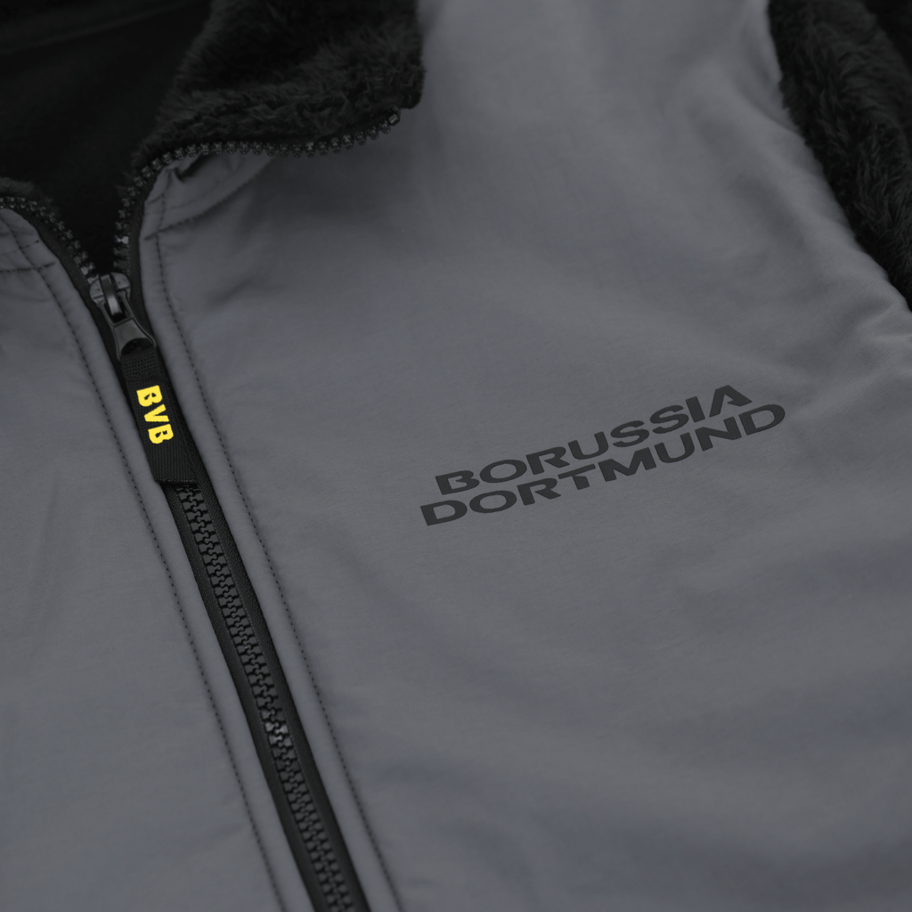 Immagine ravvicinata di una giacca nera del BVB in pile Teddy con la scritta "Borussia Dortmund" e cerniera.