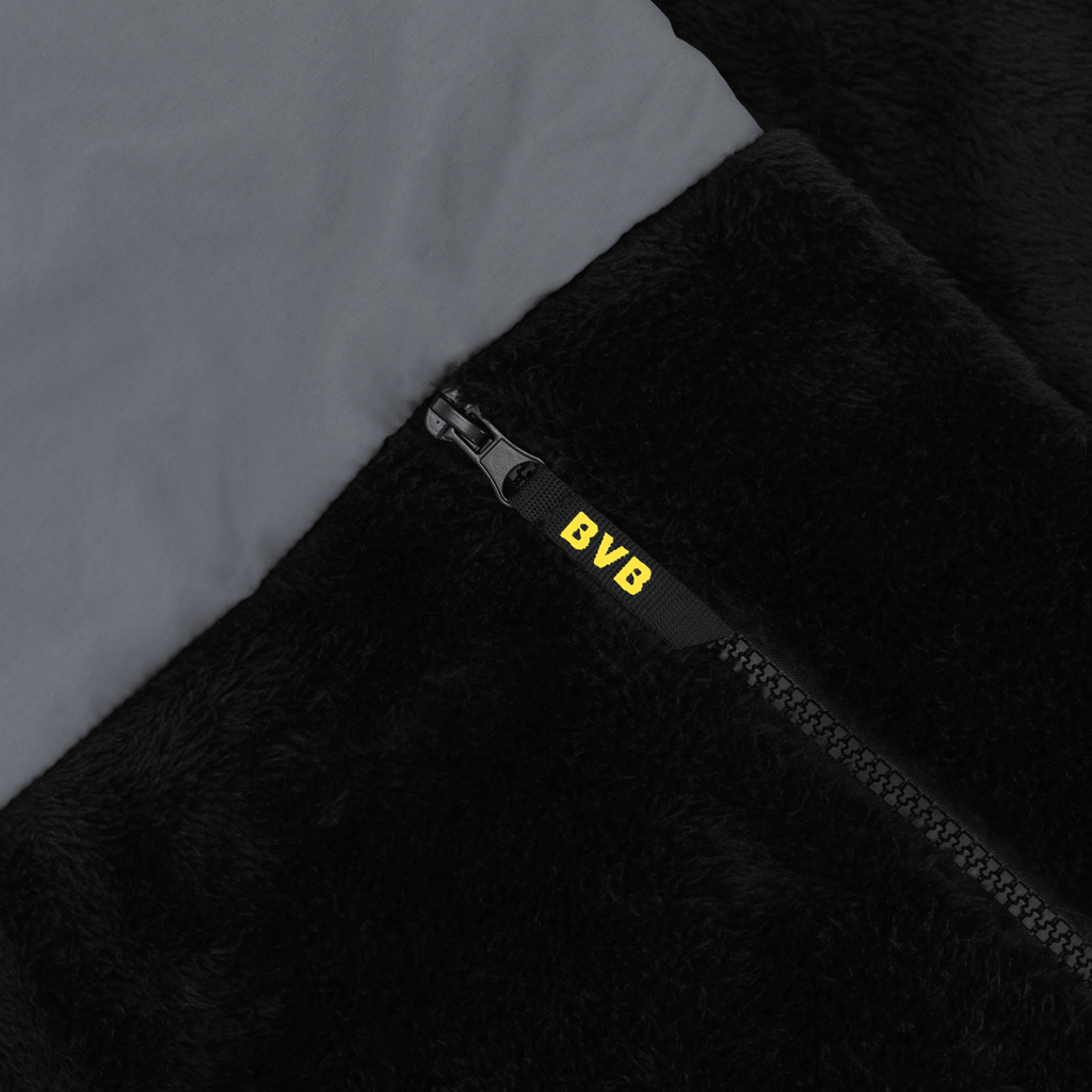 Primo piano di una giacca nera in pile con cappuccio del BVB, dotata di cerniera e con il logo giallo del BVB sulla cerniera.