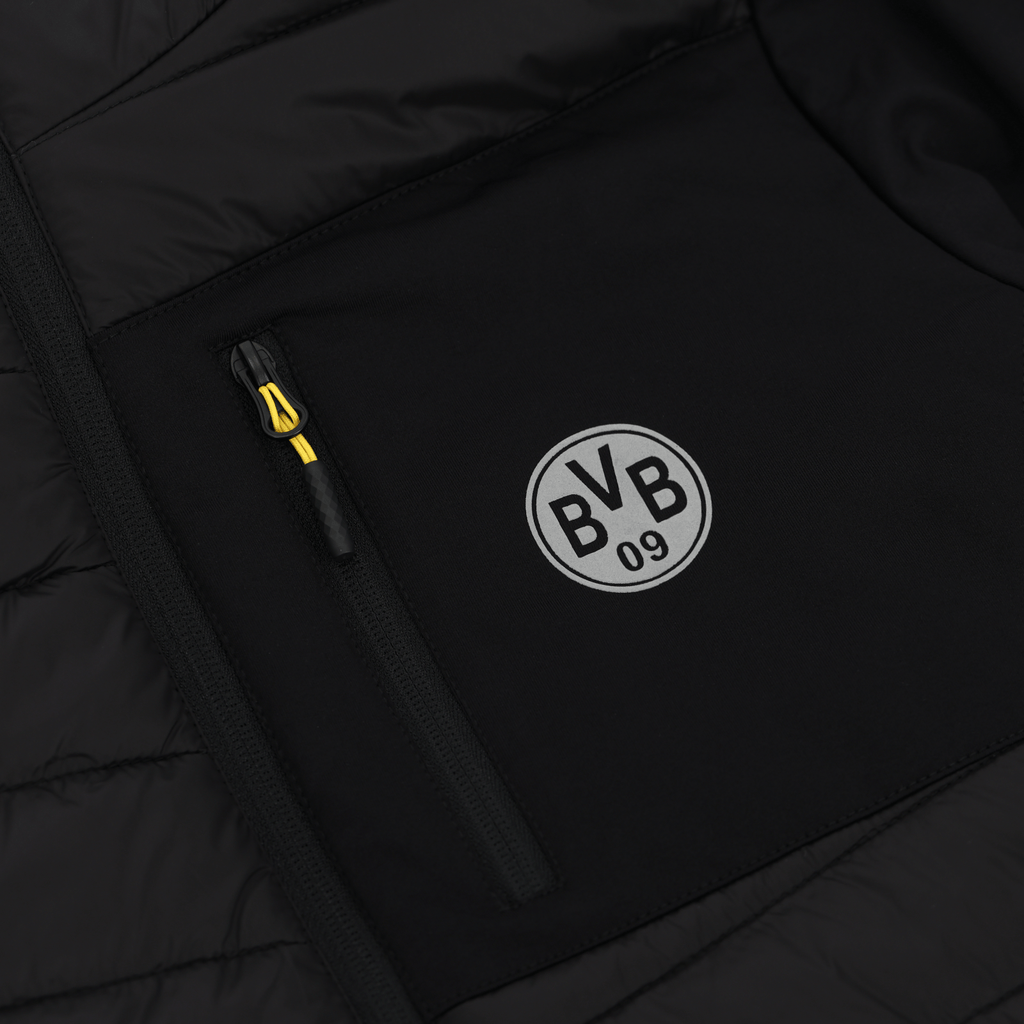 Gros plan sur la veste de stade du BVB 2025, de couleur noire, avec le logo « BVB 09 » blanc et un tirette de fermeture éclair jaune.