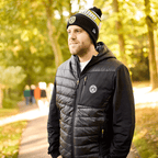 Dans un parc aux couleurs de l'automne, un homme porte la veste noire du stade du BVB 2025, ornée de l'emblème du BVB, ainsi qu'une casquette noire et jaune.