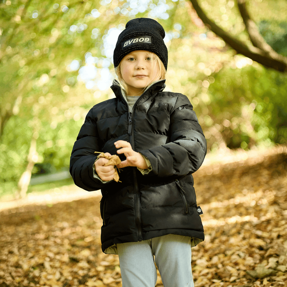 Black BVB reversible jacket for kids with a matching BVB beanie, perfect for fall and winter, modeled by a child in a fall-themed park.