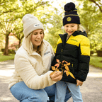 Chaqueta de invierno infantil del BVB con diseño en negro y amarillo, perfecta para actividades al aire libre, combinada con un gorro a juego del BVB. La imagen muestra a una madre y a su hija en el parque.