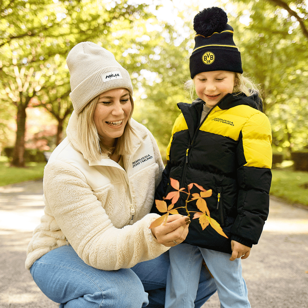 Giacca invernale per bambini del BVB con design nero e giallo, perfetta per le attività all’aperto, abbinata a un berretto del BVB coordinato. L’immagine ritrae una madre e una figlia al parco.