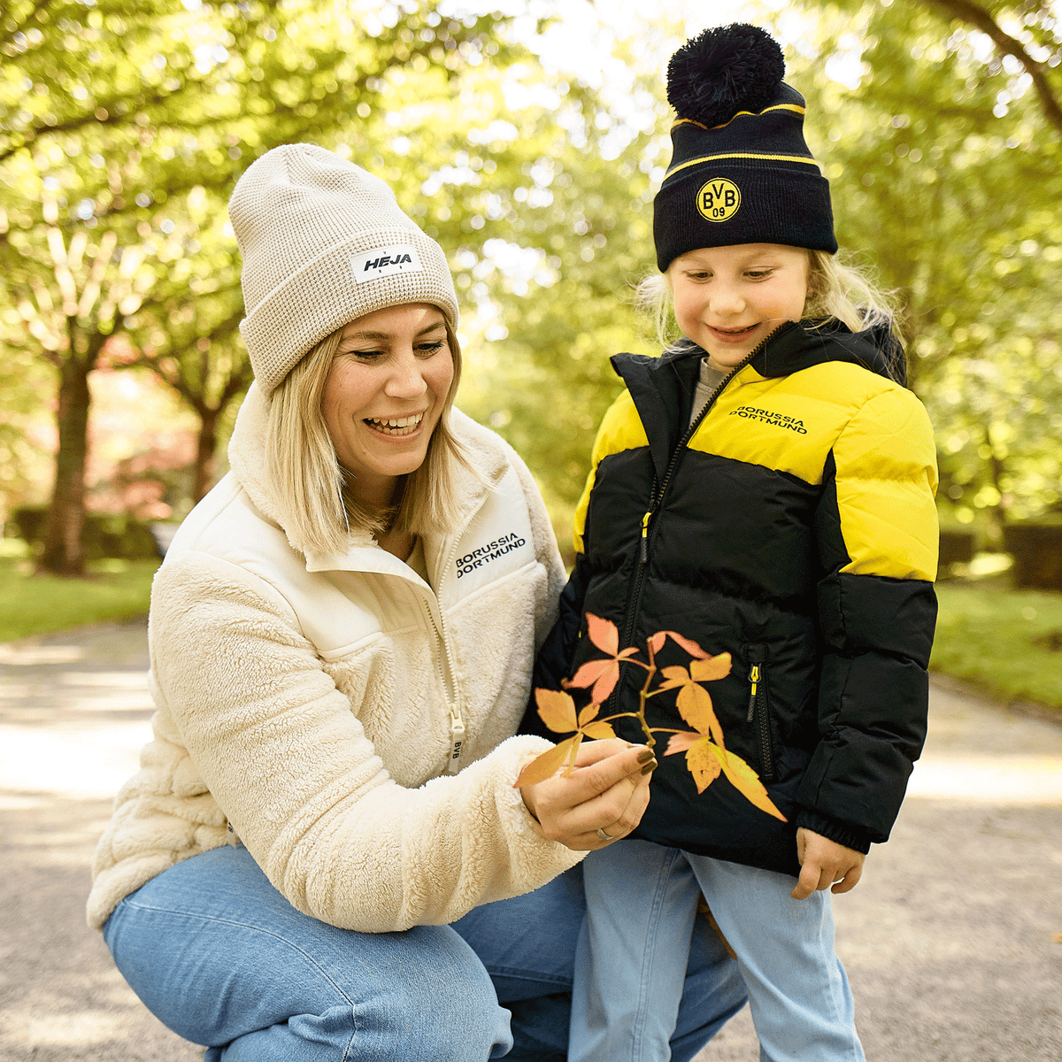 Giacca invernale per bambini del BVB con design nero e giallo, perfetta per le attività all’aperto, abbinata a un berretto del BVB coordinato. L’immagine ritrae una madre e una figlia al parco.