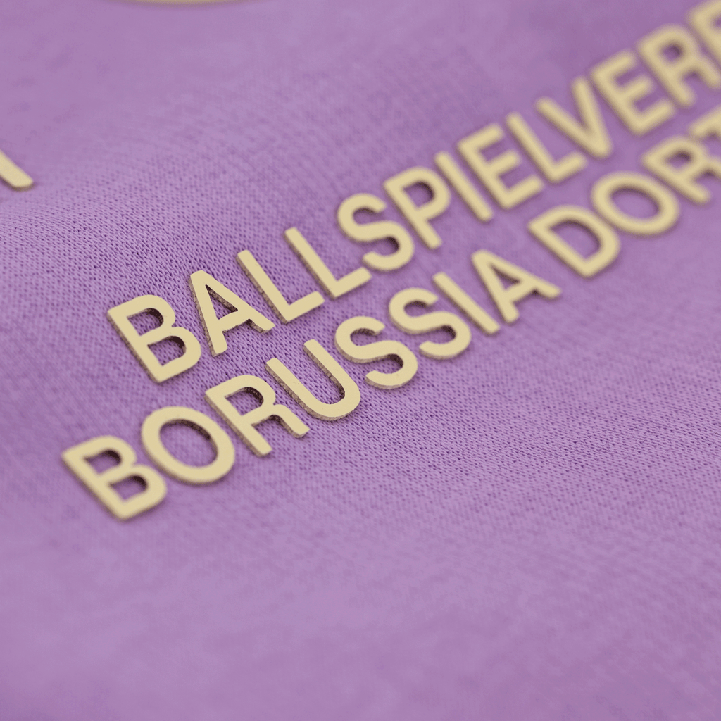 ボルシア・ドルトムントの紫色のフーディの詳細写真。金色の「Ballspielverein Borussia Dortmund」の文字が入っている。