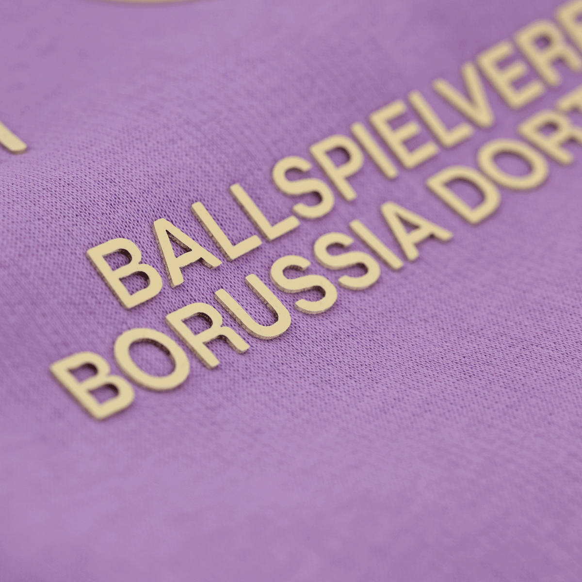 Vista dettagliata di una felpa con cappuccio viola del Borussia Dortmund con la scritta dorata “Ballspielverein Borussia Dortmund”.