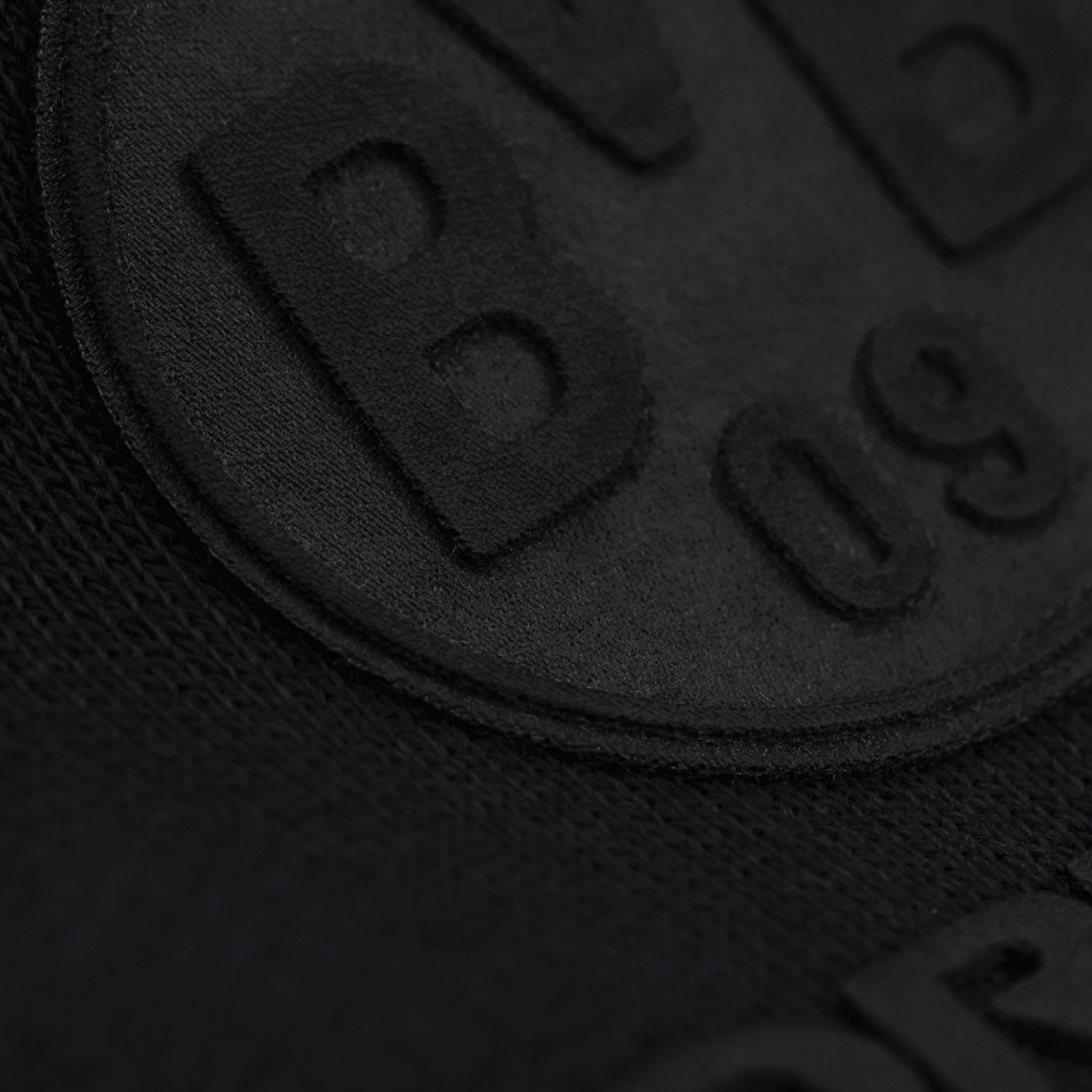 Immagine ravvicinata della felpa con cappuccio nera BVB Core con logo BVB-09 in rilievo, di colore nero su tessuto nero.