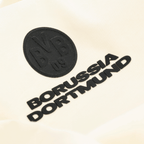 La maglietta BVB Core in colore off-white presenta un primo piano dello stemma nero del BVB e della scritta “Borussia Dortmund”.
