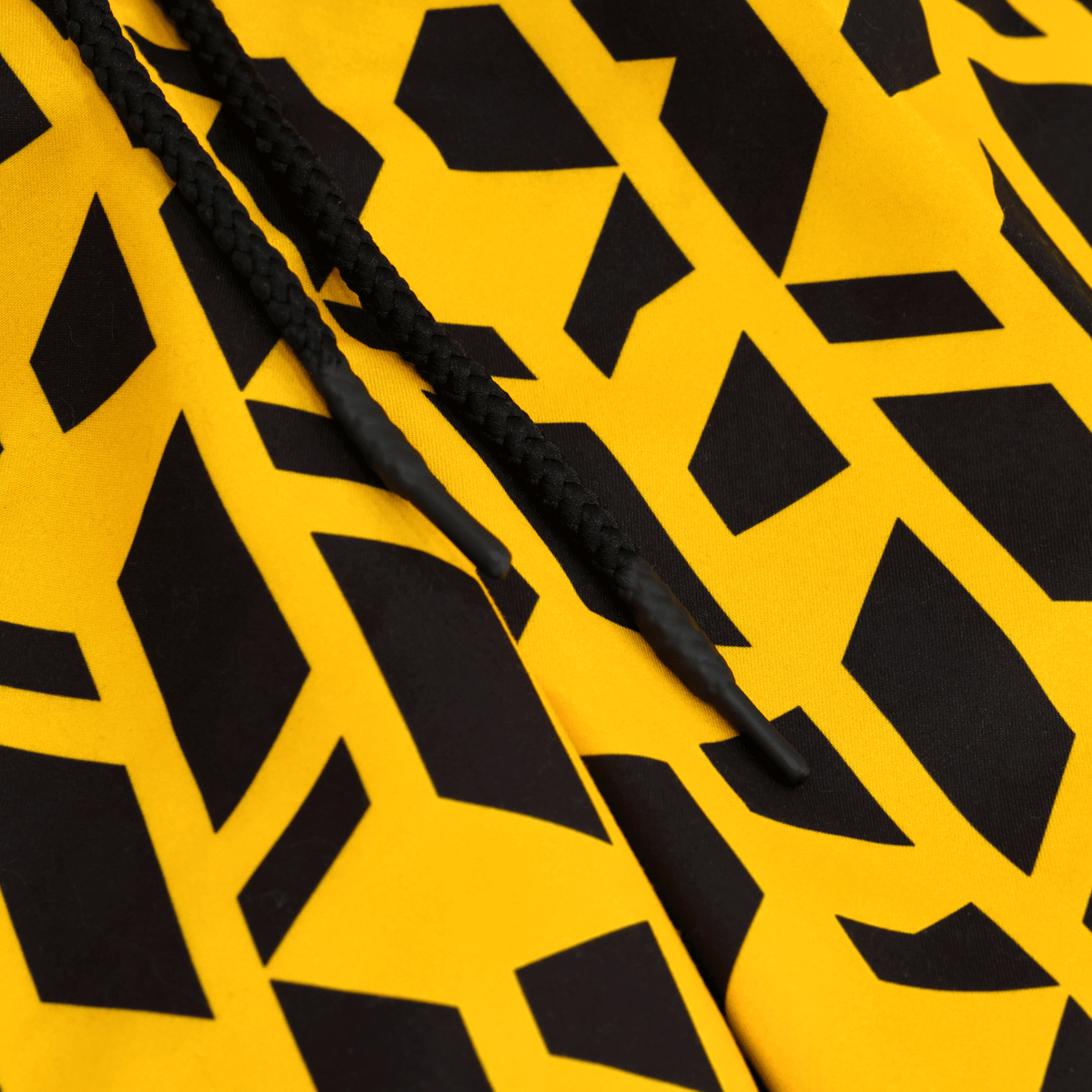Pantaloncini del BVB Festival II nei colori nero e giallo con motivo geometrico; un primo piano ricco di dettagli mostra i lacci neri.