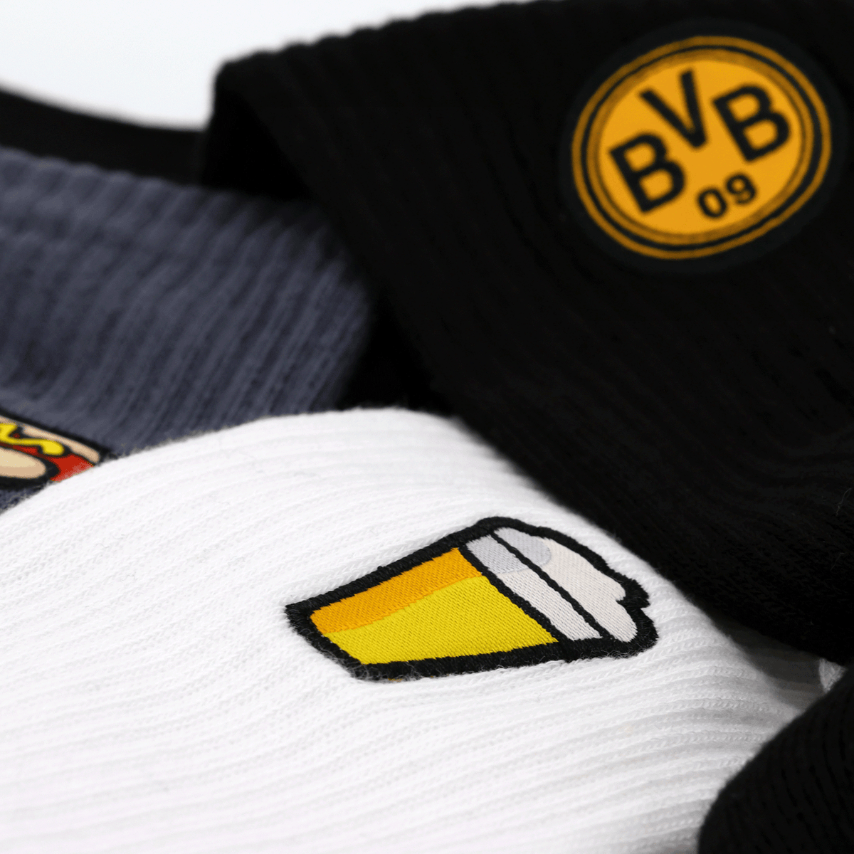 Lote de 3 pares de calcetines «BVB Festival Icons» en negro, gris y blanco, con el logotipo del BVB y motivos de cerveza y perritos calientes.