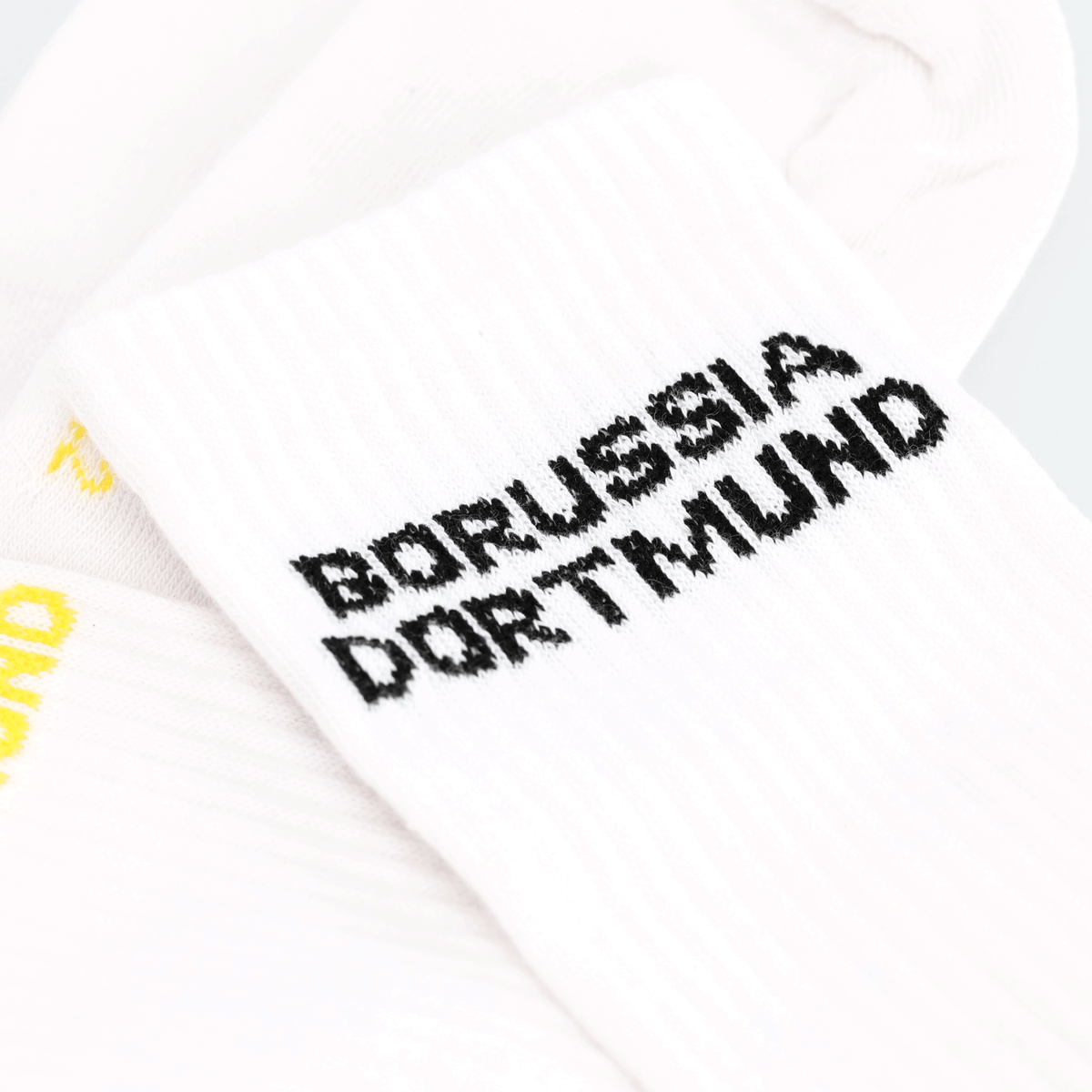 Detailaufnahme von weißen BVB Urban Socken im 2er-Set mit BORUSSIA DORTMUND Schriftzug in schwarz und gelb.