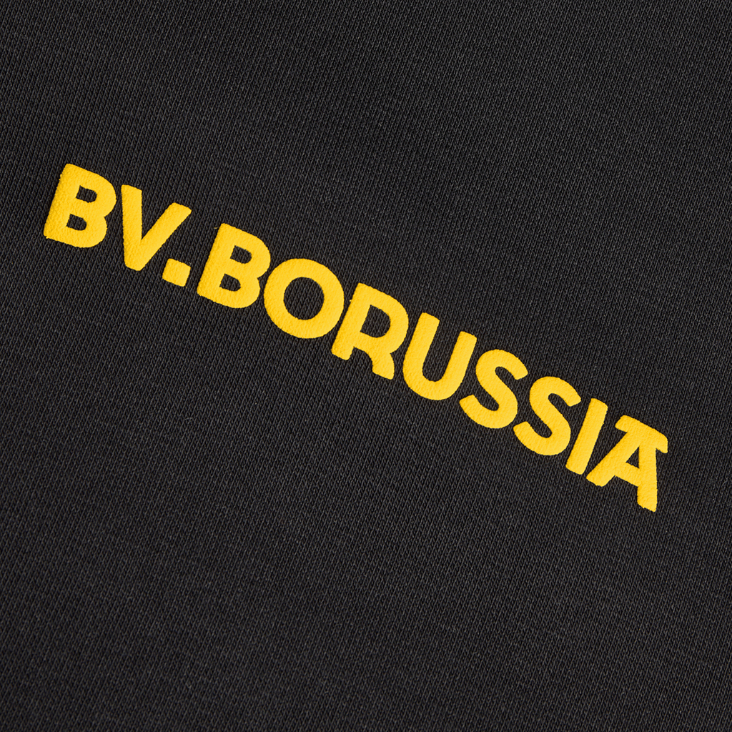 Detailansicht eines schwarzen BVB-Hoodies aus der Kollektion Rote Erde mit gelbem Schriftzug 'BV. Borussia' auf der Vorderseite.