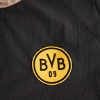 图片展示了一件黑色多功能运动夹克上的多特蒙德队（BVB）队徽特写，夹克上点缀着黄色元素。