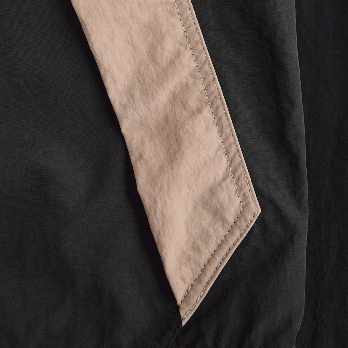 Close-up of a BVB “Rote Erde” track jacket in black and beige, focusing on the sleeve with the seam.