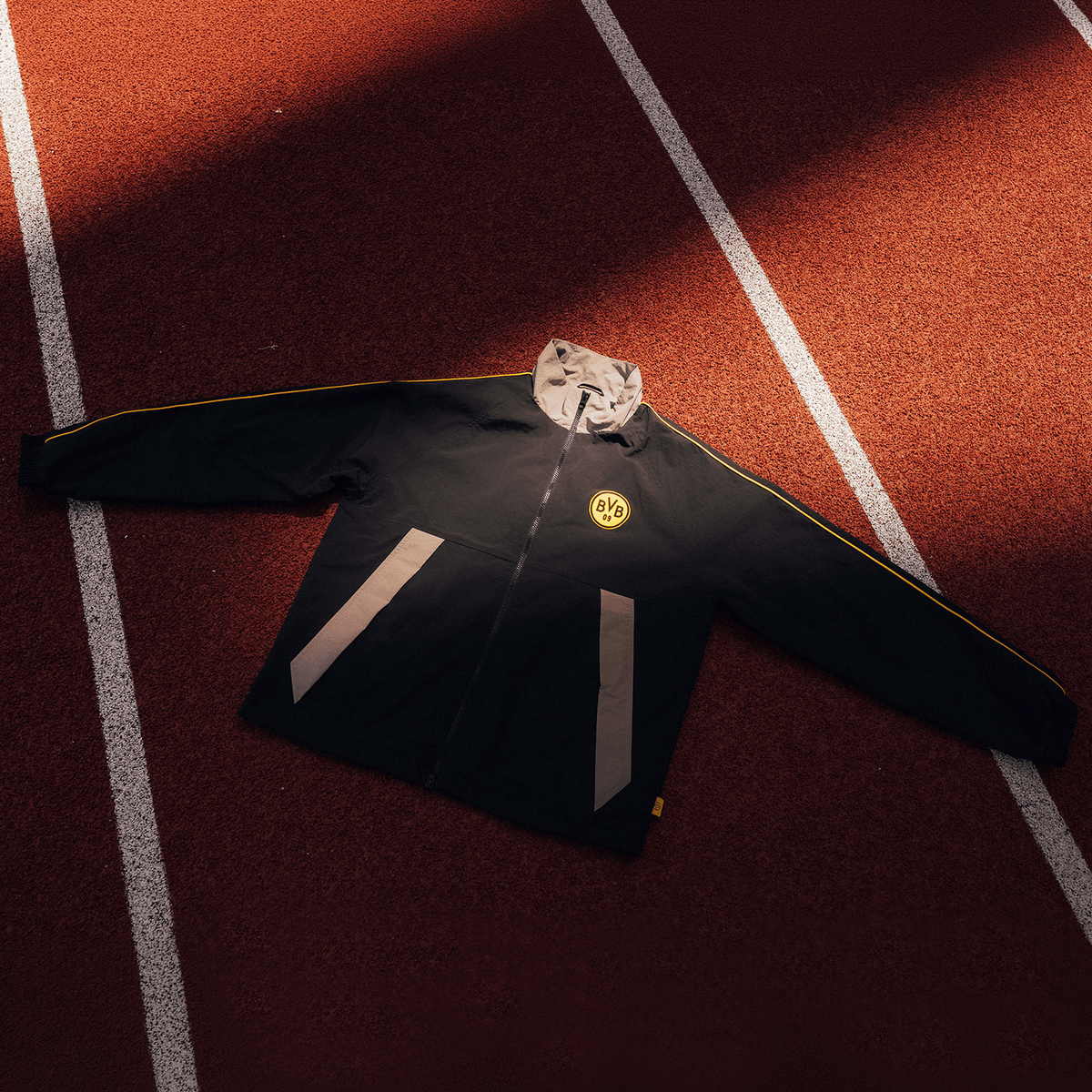 Black BVB track jacket in "Rote Erde" with yellow details and the BVB logo on the chest, photographed on a running track.