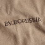 Maglietta beige del BVB con la scritta “BV Borussia” in rilievo, vista in primo piano, ideale per i tifosi del Borussia Dortmund.