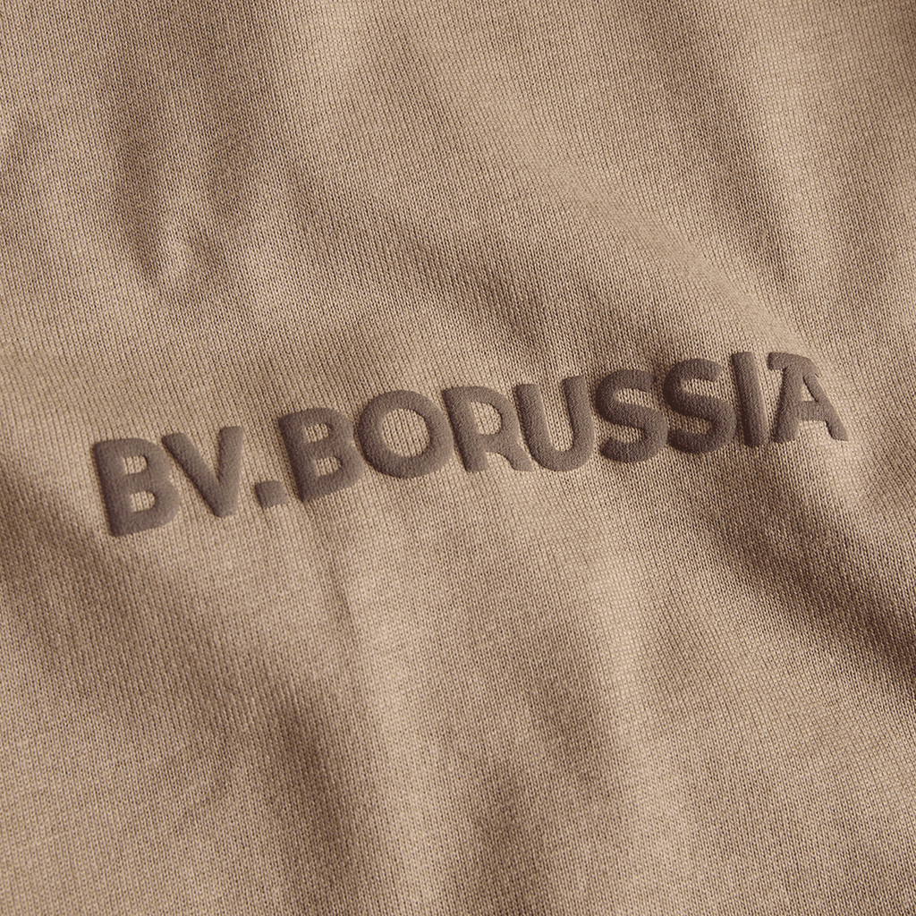 Beiges BVB T-Shirt mit geprägtem BV Borussia Schriftzug in der Detailansicht, ideal für Fans von Borussia Dortmund.