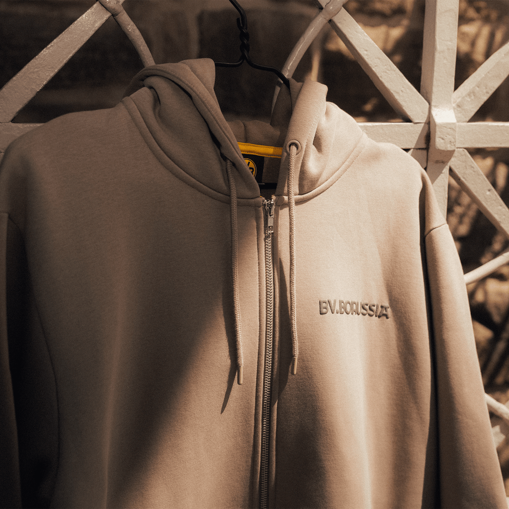 Giacca in felpa beige con cappuccio, cerniera e discreto logo BV.BORUSSIA; design moderno, ideale per i tifosi del BVB e per il tempo libero.