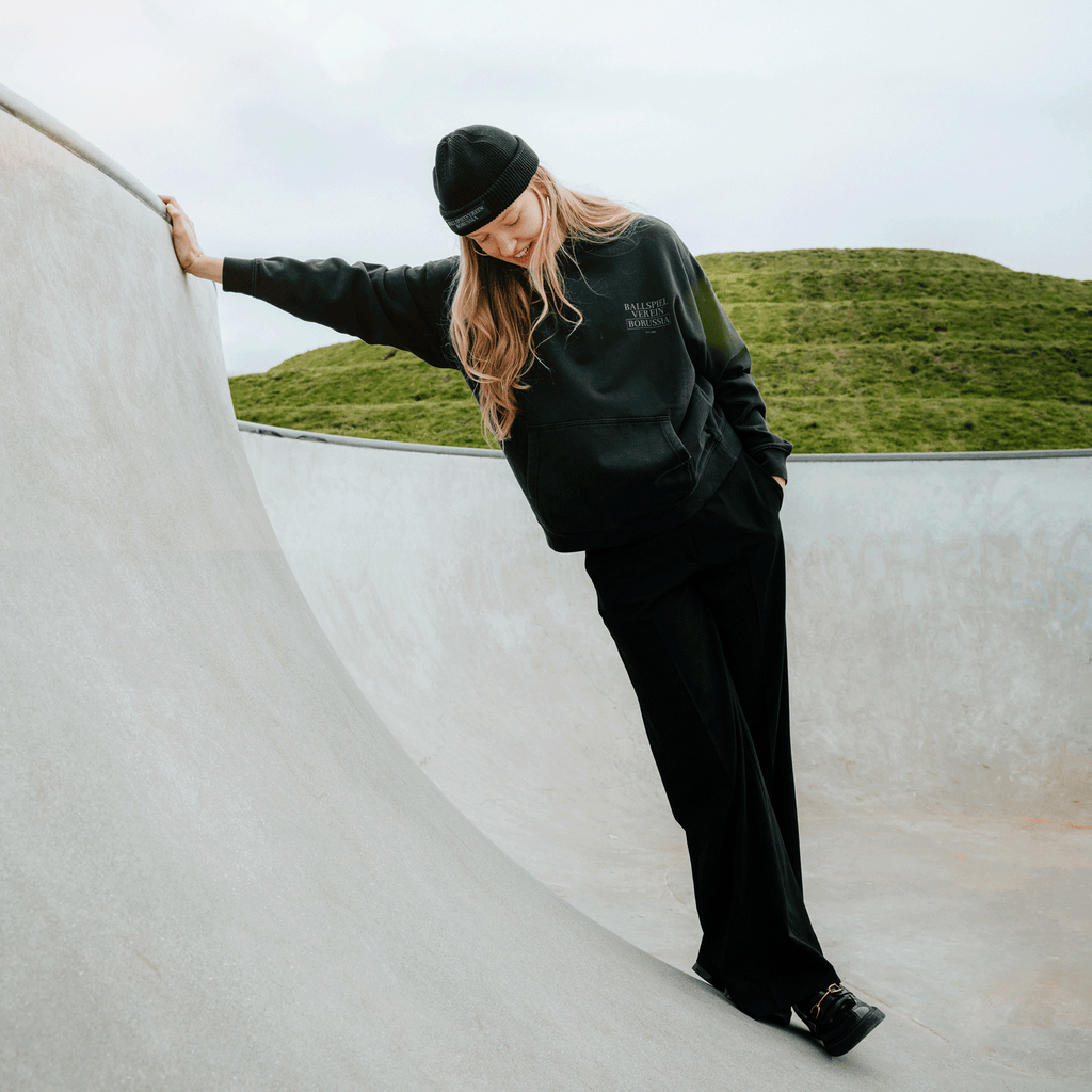 Felpa con cappuccio nera del BVB da donna in cotone lavato, indossata da una donna in uno skatepark sullo sfondo di un paesaggio verde.