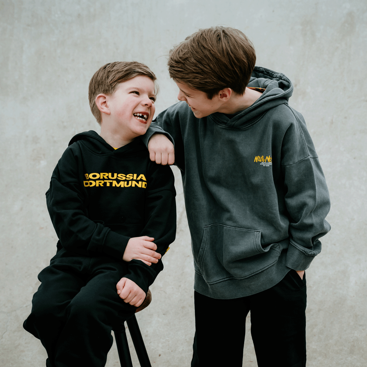 Due bambini vestiti da tifosi del BVB, con felpe con cappuccio nei colori nero-giallo e grigio, si scambiano un sorriso amichevole.