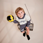 Un bambino indossa la felpa con cappuccio BVB Colorblock II nei colori grigio e bianco con il logo BVB09 e tiene in mano un pallone da calcio nero e giallo. Un articolo perfetto per i piccoli tifosi del BVB.