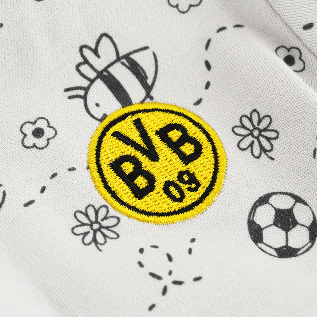 Immagine ravvicinata di un body per neonati del Borussia Dortmund con il logo BVB giallo e nero e graziosi motivi a forma di ape su tessuto bianco.