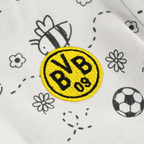 Immagine ravvicinata di un body per neonati del Borussia Dortmund con il logo BVB giallo e nero e graziosi motivi a forma di ape su tessuto bianco.