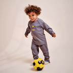 T-shirt à manches longues pour bébés et jeunes enfants, de couleur grise, avec le logo du BVB, l'inscription « 1909 » et un ballon de football jaune, représentant un enfant en train de jouer, vu de face.