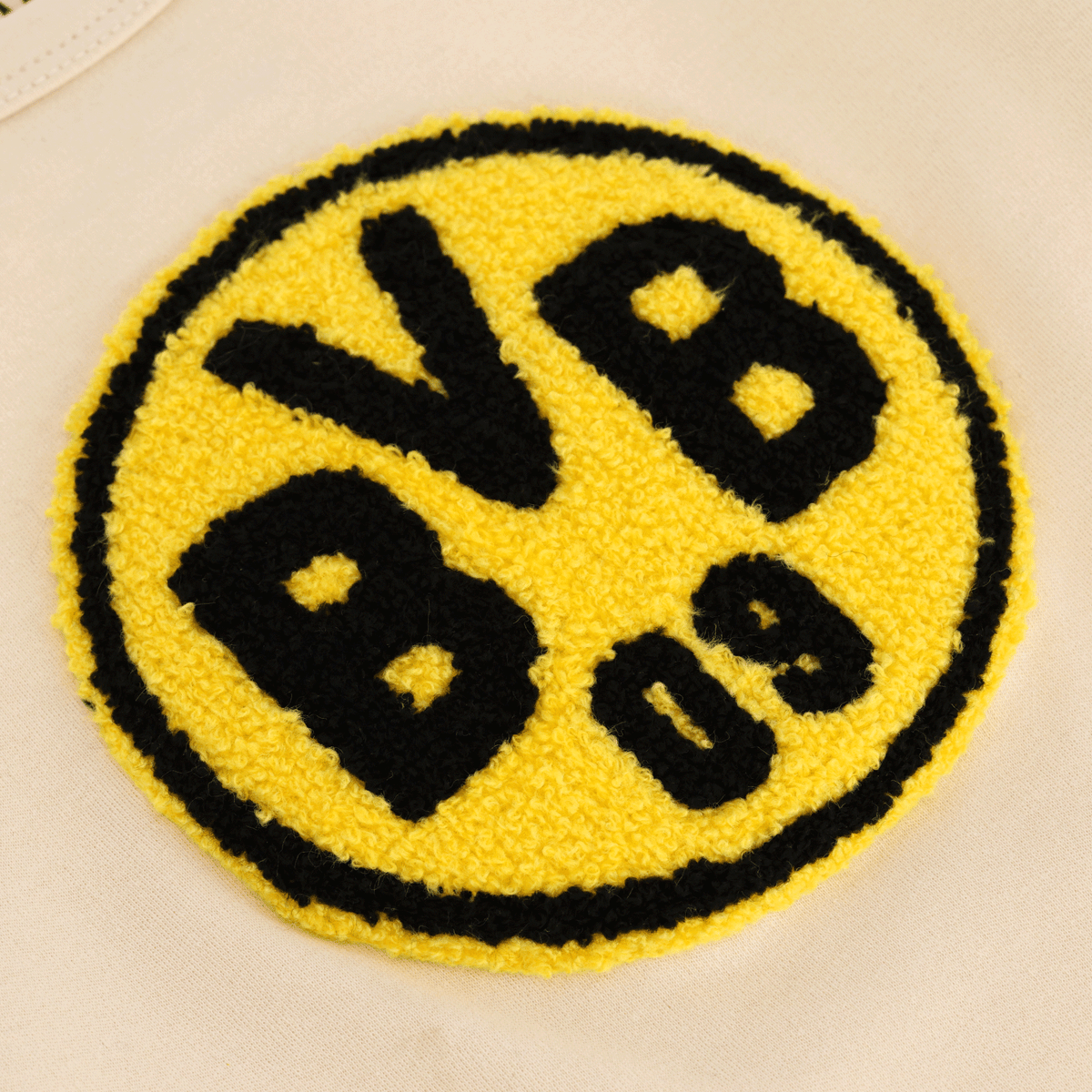 The image shows a close-up of the black-and-yellow BVB logo on a beige fabric, ideal for baby and children's clothing.