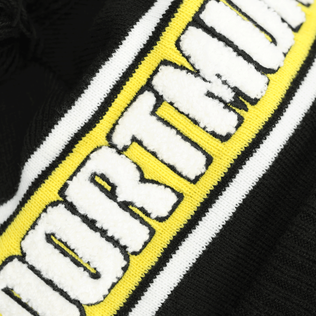 Immagine del berretto con pompon del BVB di New Era con la scritta “DORTMUND” in bianco su sfondo giallo-nero, perfetto per i tifosi in inverno.