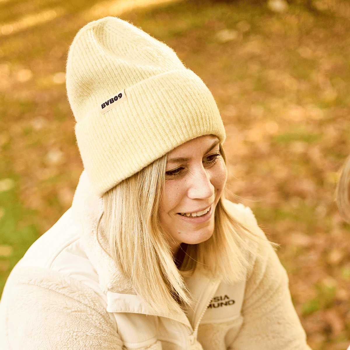 Cappellino del BVB color giallo pastello con il logo del BVB, indossato da una persona sorridente in un ambiente autunnale. L'accessorio perfetto per i tifosi del BVB.