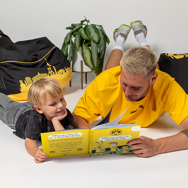 Ein gelbes BVB Mitmachbuch, das von einem Vater und seinem Sohn gemeinsam gelesen wird, perfekte Beschäftigung für BVB-Fans.