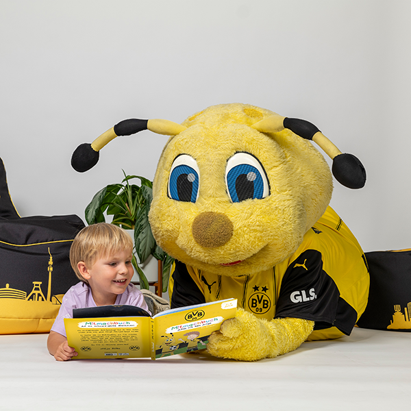 BVB-Maskottchen EMMA liest das BVB-Mitmachbuch mit einem Kind. Perfekter Fanartikel für junge Borussia Dortmund Anhänger, mit schwarzgelben Details.
