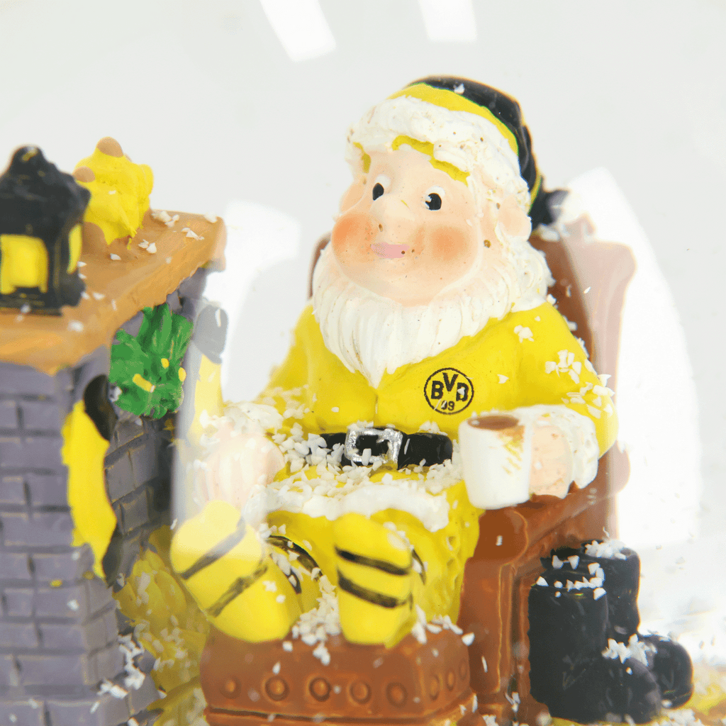 Snow globe with a BVB design, featuring Santa Claus in black-and-yellow attire sitting in front of a fireplace with a mug, surrounded by snowflakes.