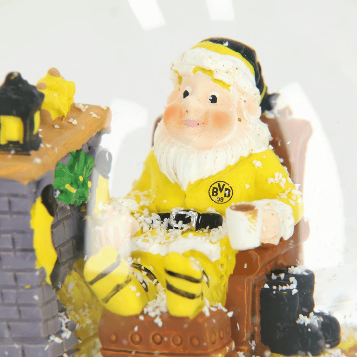Snow globe with a BVB design, featuring Santa Claus in black-and-yellow attire sitting in front of a fireplace with a mug, surrounded by snowflakes.
