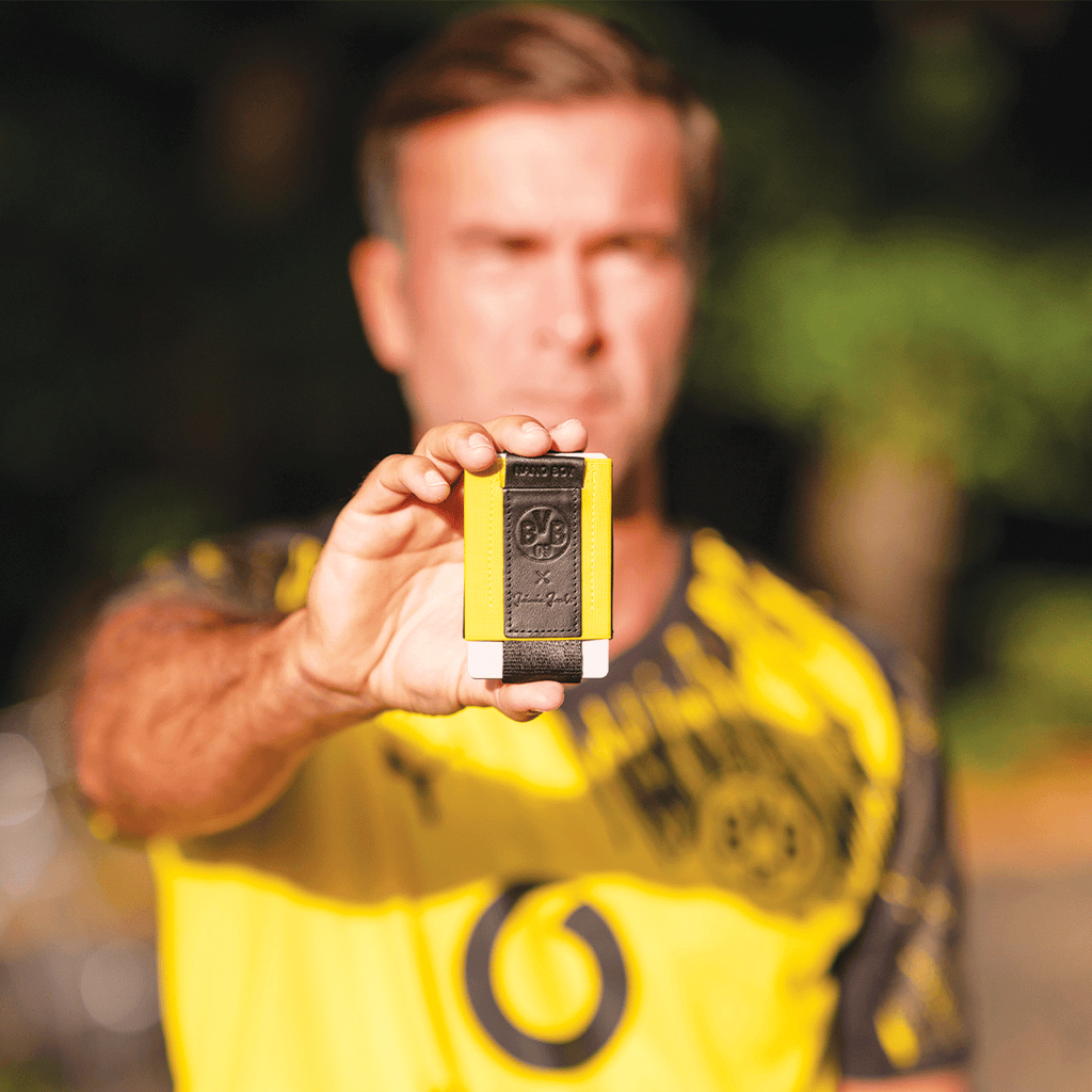 Porte-monnaie BVB Nano Boy Pocket aux couleurs noir et jaune, maniable et pratique, avec en arrière-plan une personne portant un maillot du BVB.