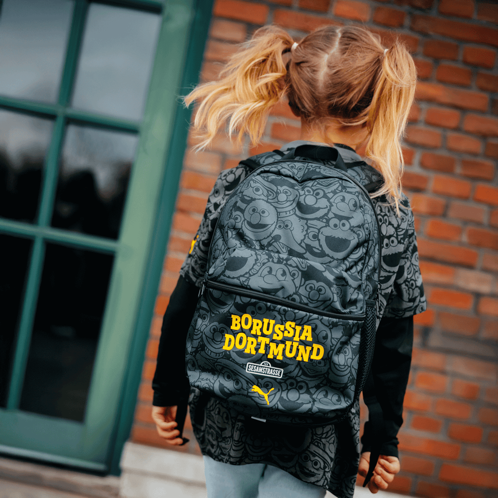 Un enfant porte un sac à dos « BVB-Sesame Street » orné de personnages de Sesame Street aux couleurs noir et jaune et portant l'inscription « Borussia Dortmund ».