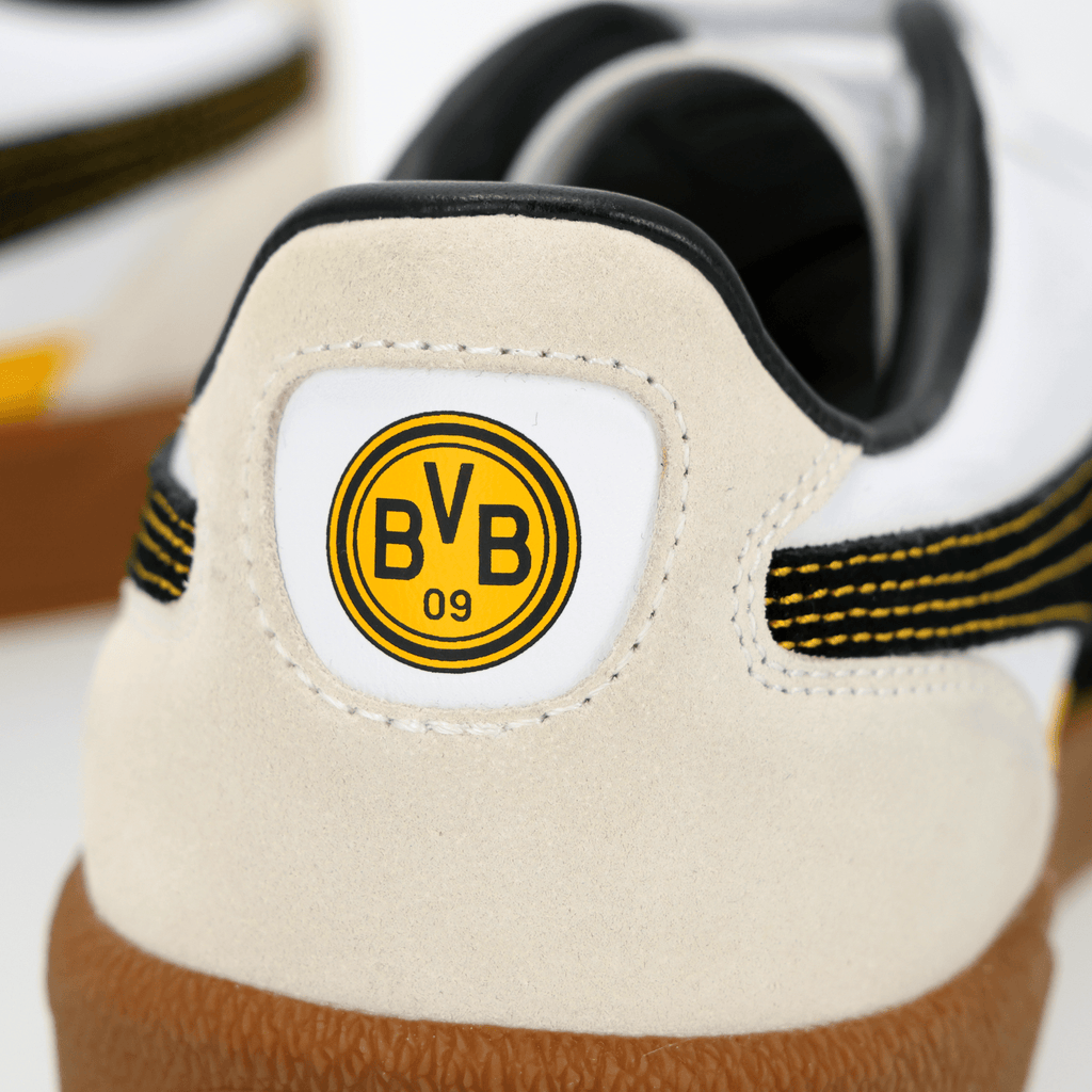 Close-up view of a pair of BVB Puma Palermo sneakers with a white upper, black-and-yellow stripes, and the BVB 09 logo on the back.
