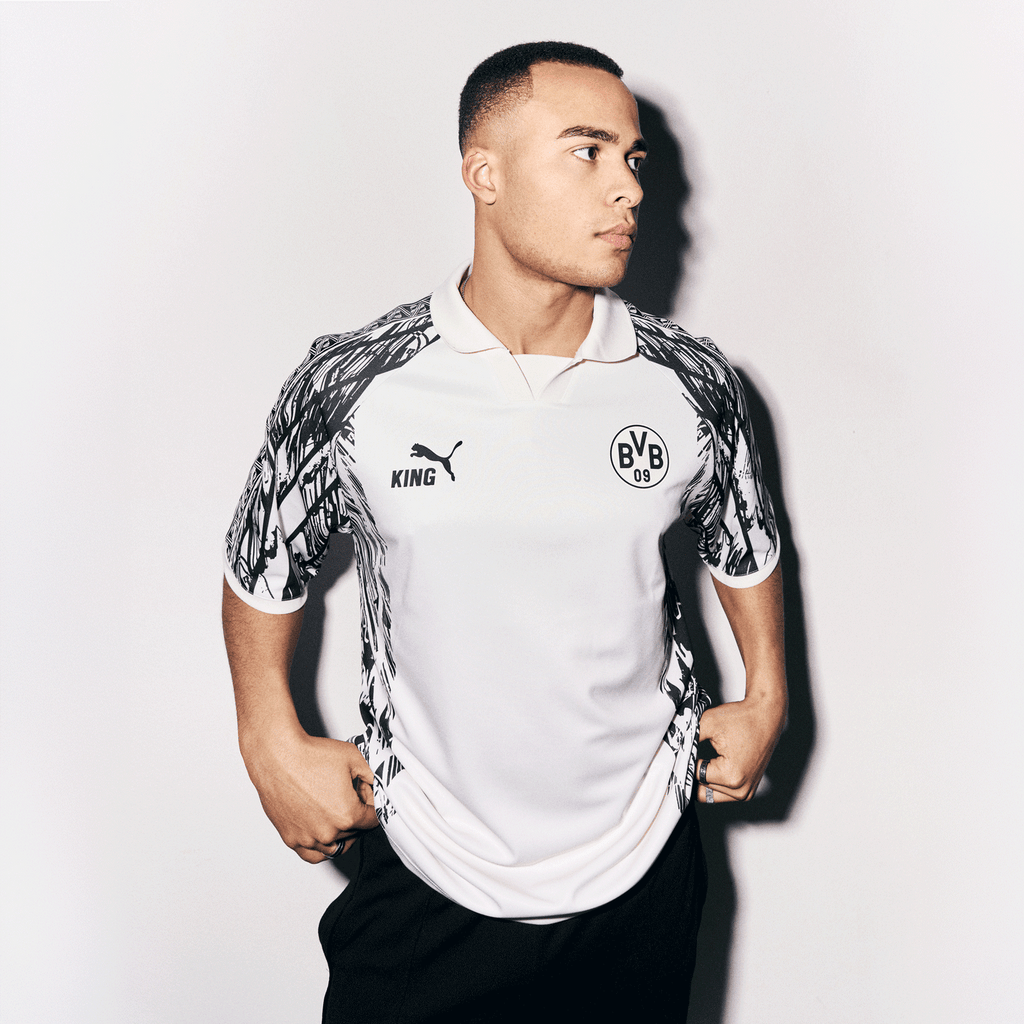 Maglia del BVB "King" bianca e nera con il logo della squadra sul petto, il logo PUMA e un design sportivo, indossata da un uomo in una foto frontale.
