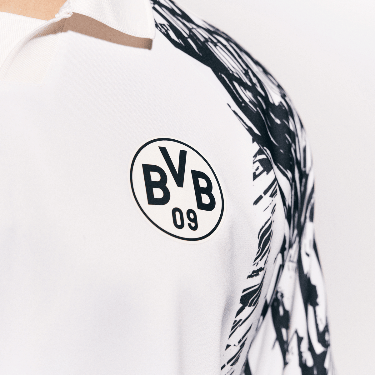 Primo piano della maglia bianca del BVB King con il logo nero "BVB 09" sul petto e un motivo astratto in bianco e nero sulla spalla.